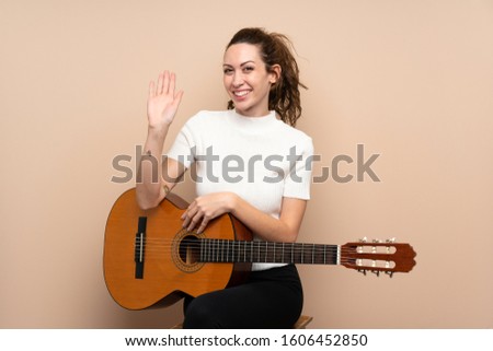 Young woman with guitar over isolated background saluting with hand with happy expression