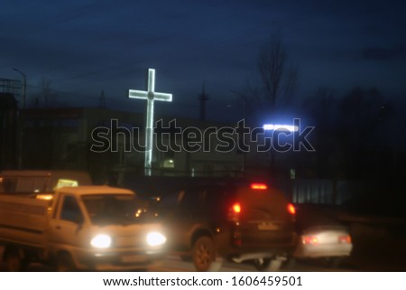 Christian, a large cross with white LED backlight on a highway with vehicles under a blue, summer sky.  Night blurred background