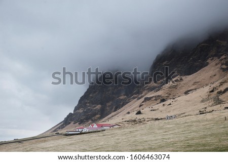 in the distance a lonely white house with a red roof on a background of mountains, fog and overhanging clouds