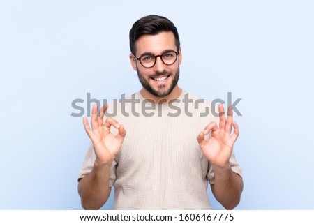 Young handsome man with beard over isolated blue background showing an ok sign with fingers