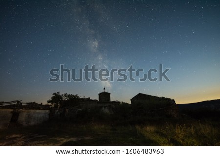 Milky way over the silhouette of a town in the night with an iridium flare acrossing the sky