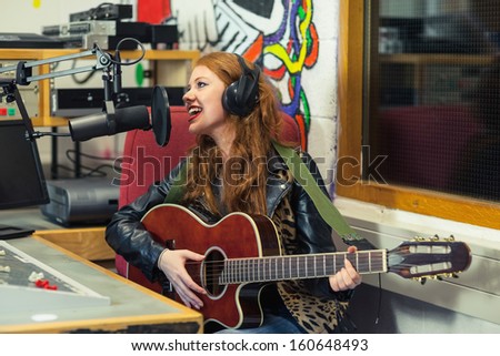 Cheerful beautiful singer recording and playing guitar in studio at college