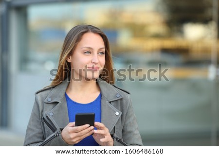Front view portrait of a confident woman holding mobile phone looking at side in the street