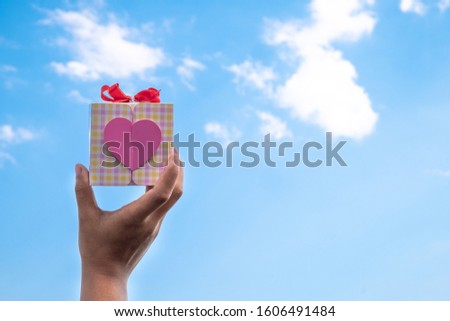 A hand holding a gift box with a heart shape. Concept of Love, holidays, valentine's day.