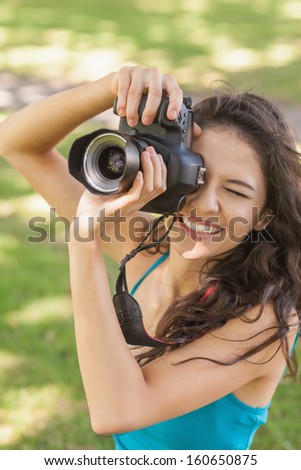 High angle view of cheerful young woman taking a picture in a park