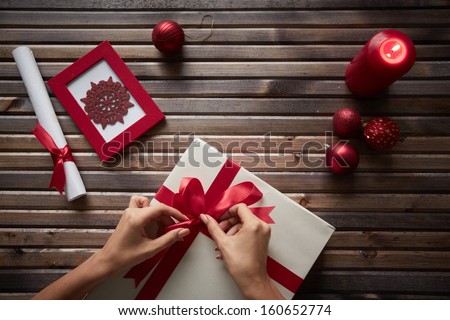 Image of female hands tying knot on giftbox surrounded by Christmas symbols