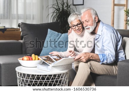Romantic senior couple laughing while sitting on sofa at home and watching old pictures together