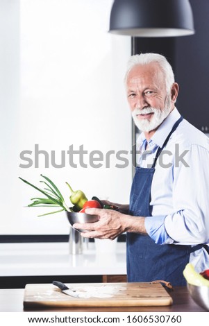 Portrait of senior bearded handsome man standing at the kitchen  cooking vegetables for lunch and looking at camera. Copy space picture