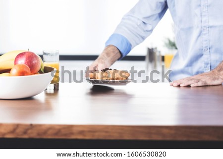 hands of man holding dish with chocolate croissant for breakfast. Orange juice and bowl with fruits on wooden table. People, morning, breakfast and food concept. Wallpaper picture with space for text