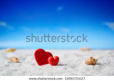 Beautiful two red hearts on white blurry sand beach over blurred blue sky background used for your design, for lover romantic symbol. Holiday, summer and valentine's day concept.
