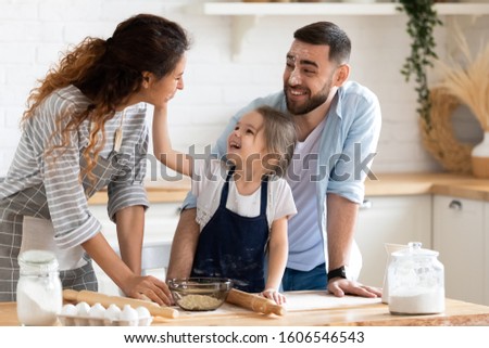 Cheerful husband wife and cute pre-school daughter preparing pie, playing together enjoy pastime and common hobby on domestic cozy kitchen feels happy, ideal beautiful family at home cooking concept