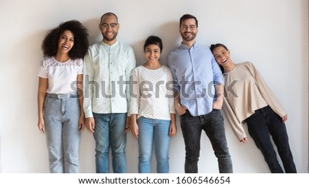 Happy multiethnic young people stand in row look at camera posing for group picture together, funny international millennial friends laugh having fun show unity and support, friendship concept