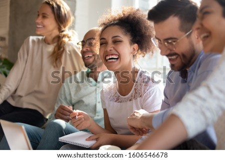Overjoyed multiracial young people sit in row have fun laughing studying together indoors, happy international diverse students joke chat brainstorm preparing for test making notes learning Royalty-Free Stock Photo #1606546678