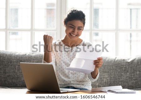 Excited indian young woman sit at home couch feel euphoric read good news in post letter, happy ethnic millennial girl receive pleasant notice in postal correspondence, reward, success concept Royalty-Free Stock Photo #1606546744