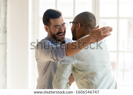 Smiling Caucasian man in glasses feel overjoyed meeting ethnic male friend or colleague, happy young multiethnic guys hug embrace tapping shoulder excited encounter at party, friendship concept Royalty-Free Stock Photo #1606546747