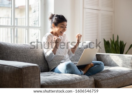 Overjoyed millennial indian girl sit on couch at home feel euphoric get pleasant online message, excited young ethnic woman triumph win lottery on computer, receive unexpected good news or email Royalty-Free Stock Photo #1606546759