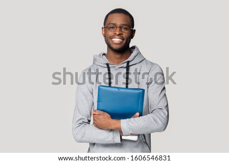 African student pose isolated on grey studio background smiling looking at camera holding in hands folder educational material, first day in university, higher education, exams and test passed concept