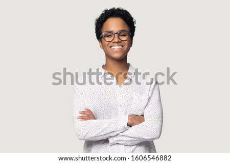 Attractive African ethnicity woman wears casual blouse and glasses pose isolated on gray background standing with arms crossed having wide beautiful smile looks at camera feels confident and healthy