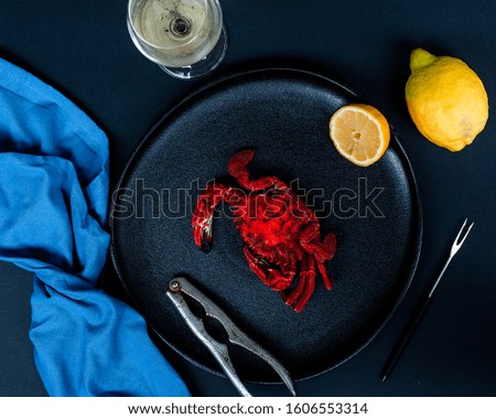 Cooked hard shell crab on a black plate with pincers contrasting with bright yellow lemon, blue napkin and a glass of white white.
