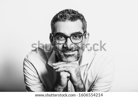 Black and white portrait of handsome man wearing blue shirt and glasses, leaning on hands, posing on white background