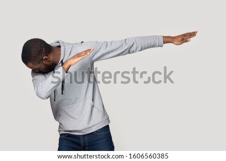 African guy makes dab, perform dabbing dance move point one arm towards aside while bowing head into other hand isolated on grey copy space wall, youth culture gesture, have fun or celebration concept