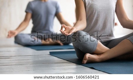 Close up young people wearing sportswear practicing yoga at group lesson, sitting in Easy Seat pose with mudra on mats, doing Sukhasana exercise, stress relief, working out in modern yoga center club Royalty-Free Stock Photo #1606560421