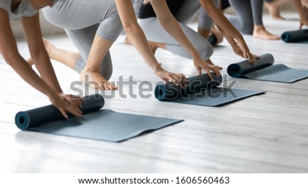 Diverse young people wearing sportswear folding yoga mat on floor in yoga studio close up, finishing group lesson holding rubber carpets, preparing for sport training in fitness center Royalty-Free Stock Photo #1606560463