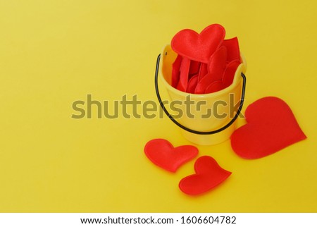 Yellow plastic bucket with red hearts on a bright yellow background. Preparing for Valentine's Day. The symbol of love. Free space for an inscription