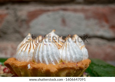 Lemon meringue tart on a green plate with pomengranate seeds and fresh mint leaves for decoration.