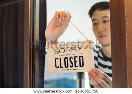 Through glass view of Asian male business owner hanging up sign with inscription closed at end of working day