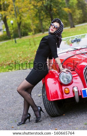 Woman in black posing on red car front