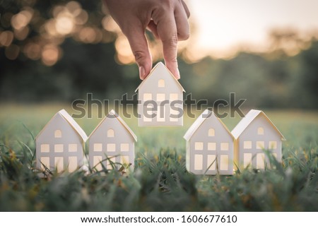 Hand choosing white paper house model from group of house on green grass, selective focus, Planning to buy property. Choose what's the best. A symbol for construction ,ecology, loan concepts Royalty-Free Stock Photo #1606677610