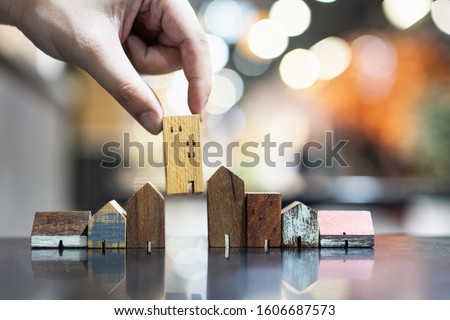 Hand choosing mini wood house model from model on wood table, selective focus, Planning to buy property. Choose what's the best. A symbol for construction ,ecology, loan concepts