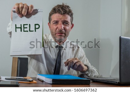corporate business worker in stress - young attractive stressed and desperate businessman holding sign crying for help overworked and overwhelmed working at office computer desk frustrated