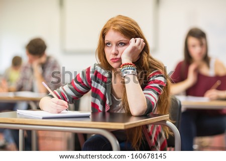 Bored young female student with others writing notes in the classroom