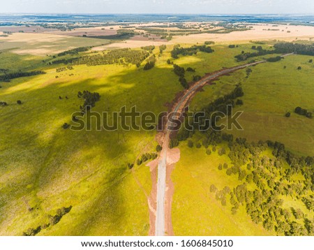 Aerial view on road under construction, among forests, fields and villages. Road works in forest and in fields. Dirt road in an open area. Railroad construction through fields and meadows