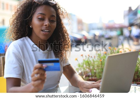 Happy attractive woman using credit card and laptop in cafe outdoors.