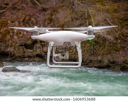 	
Geneva / Switzerland - 10/10/2019 : A drone hover in flight in front of the camera with landing lights flashing and motors spinning on a misty forest path and mountain river.