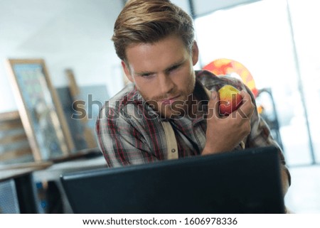 picture of male worker holding apple fruit checking laptop