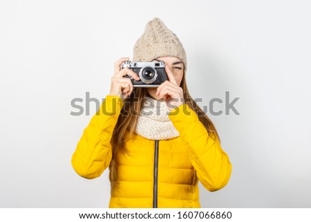 Young woman in a yellow down jacket and hat holds a camera in her hands and takes a picture on a light background. Concept of beauty and fashion, winter, autumn, technology. Banner