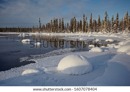 Northern landscape with non-freezing river and snow drifts against a blue sky, in the winter time, during the day. Lots of snow in the form of round caps