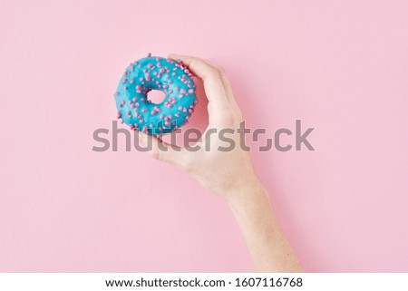 Woman hand take color donut on pink background. Creativity minimalism style food concept, top view