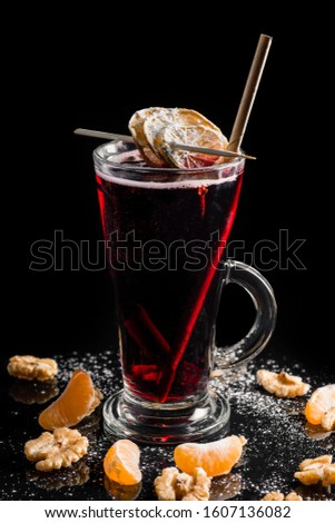 A warm drink, grog, vodka, with red color and tangerines around the glass, covered with powdered sugar. On a black background and a paper straw in the drink from a bar. Famous cocktail in europe. 
