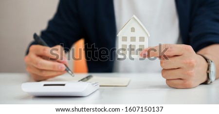 close up young man hand holding house's model and writing summary expense of home loan mortgage for refinance plan , people lifestyle concept