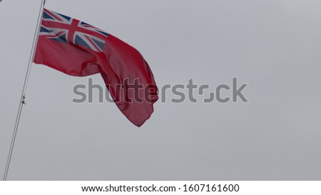 The Red duster Flag otherwise know as Red Ensign, flying in the sea breeze. The union Jack is in the top left corner. The flag is on the left hand side with negative space to the right in grey.