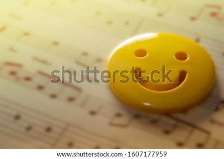 soft focus yellow emoticon smiley face icon symbol on blurred vintage music notes paper background with copy space, for hope and a positive mindset in business and for beautiful world peace concept