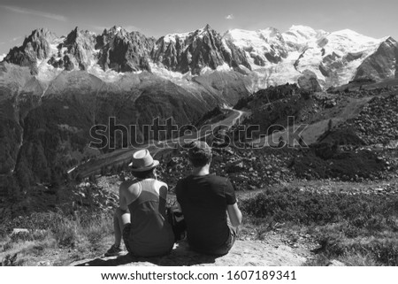 French Alps summer travel. Couple (unidentified people, back view) of hikers admiring beautiful snow covered Mont Blanc mountains range. France nature background. Travel concept.  Black white photo.
