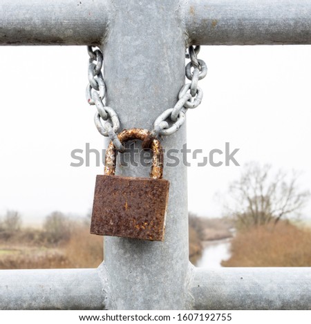 Close up view of  rusty lock with chain hanging on a grey railing. 