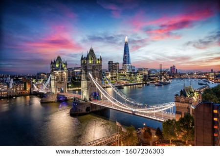 Aerial, panoramic view to the lit Tower Bridge and skyline of London, UK, along the Thames river during dusk time
