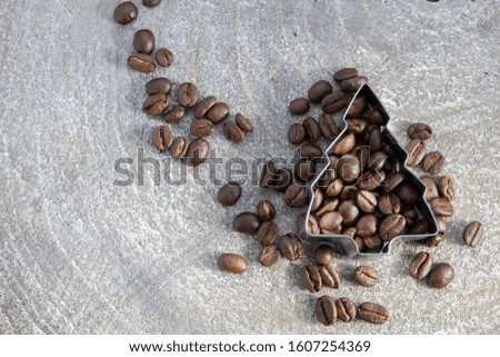 brown coffee beans filled into a cookie cutter form, shaped as christmas tree onto a rustic wooden background with spreaded beans